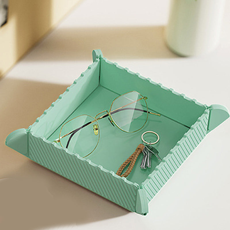 Folded mint green silicone tray holding a pair of glasses and keys